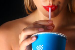 A woman with red lipstick drinking a beverage from a blue cup