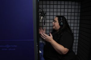 AI Voice Actor recording in a sound isolation booth wearing headphones and sitting in front of a microphone.